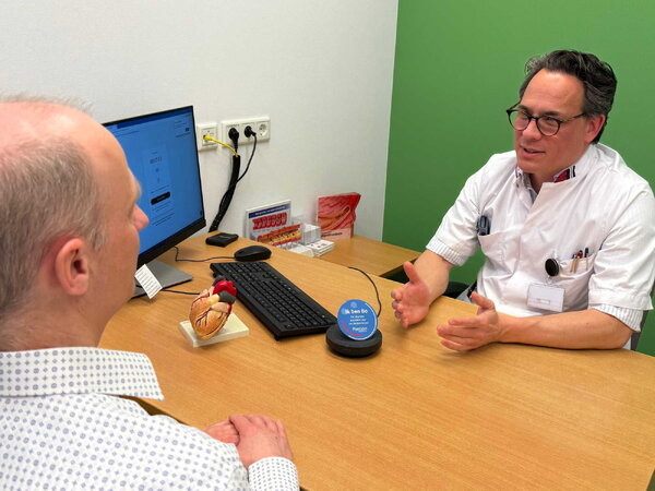 Cardioloog Bart Driesen in gesprek met patiënt, digitale assistent Bo luistert mee